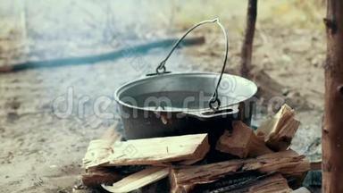 在篝火旁用旅游锅煮远足食品。 准备野营食品